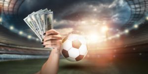 close-up-man-s-hand-holding-us-dollars-against-background-stadium-concept-sports-betting-making-profit-gambling-208405993